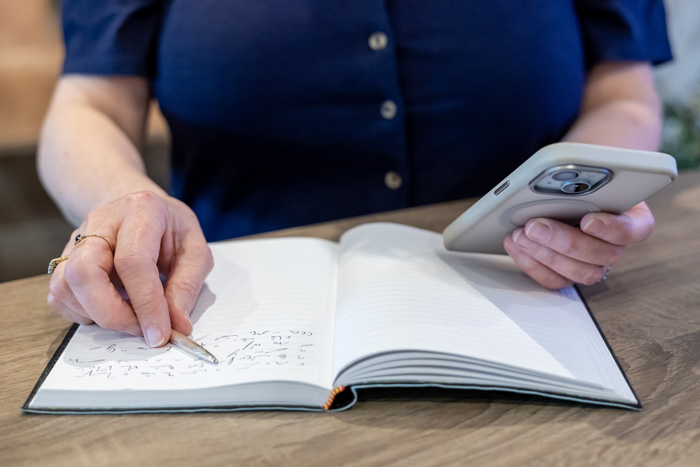 Alison Harmer's hands holding a pen and mobile over a notebook