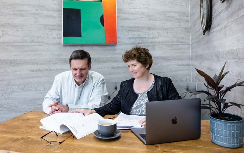 Newsletter writer Alison Harmer sat next to a man at a desk with paperwork