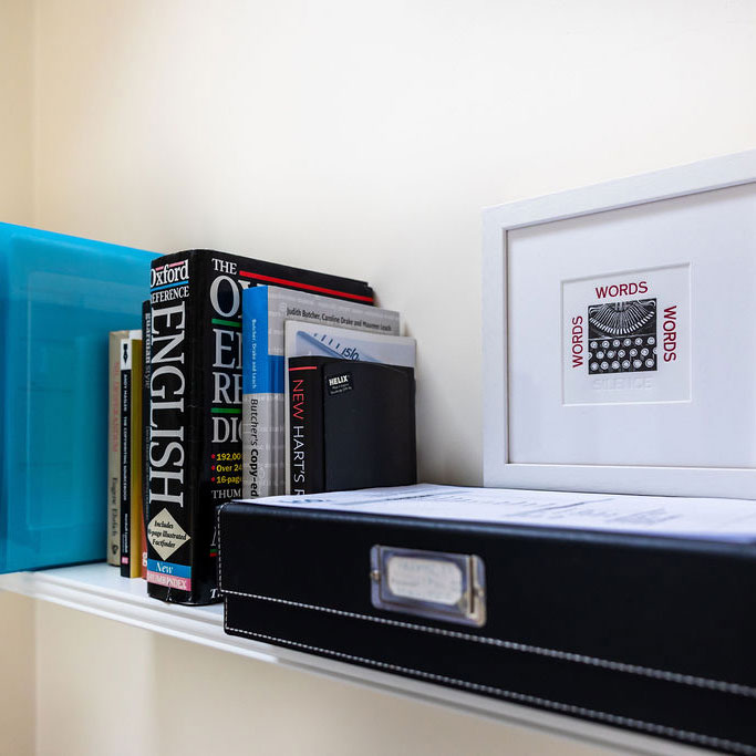 Single bookshelf with editing and proofreading books and a picture of a typewriter