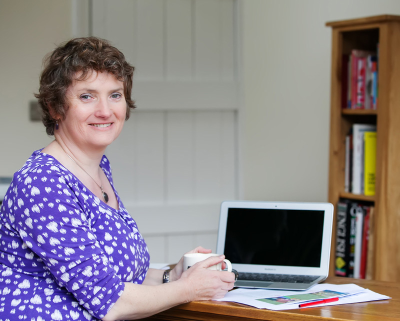 Marketing copywriter, Alison Harmer in blue top sat at desk