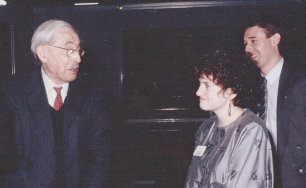 Freelance copywriter Alison Harmer in a silk grey blouse talking to scientist Dr Magnus Pyke standing with a cane and a printer a a print show in the 1980s.